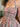 A close-up of a woman wearing a sleeveless smocked dress with a dusty peach base and a green and pink floral print.